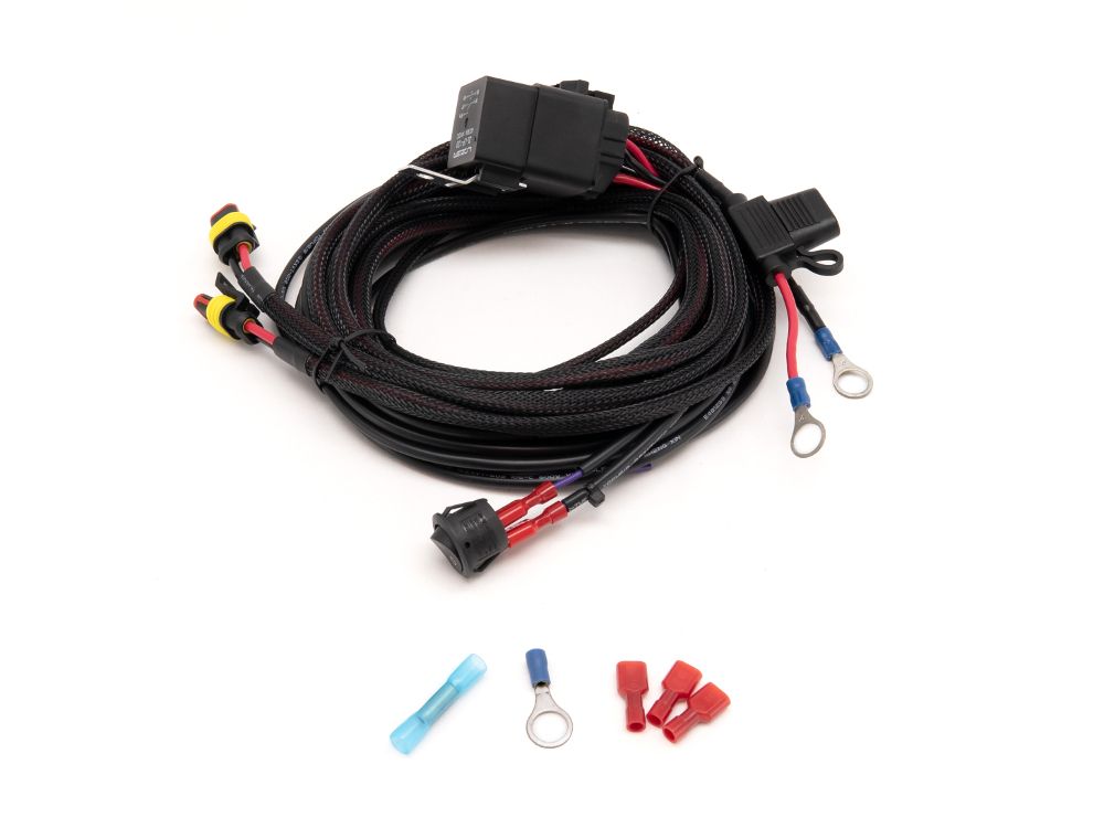 Lazer two-lamp wiring harness coiled on a white background, with the relay and blade fuse holder in the middle of the loom, two sealed lamp connectors at one end, ring terminals for the battery at the other, and the supplied heatshrink butt splice, ring terminal and spade terminals laid out below