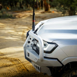 White off-road vehicle with a front bumper and antenna on a dirt road.