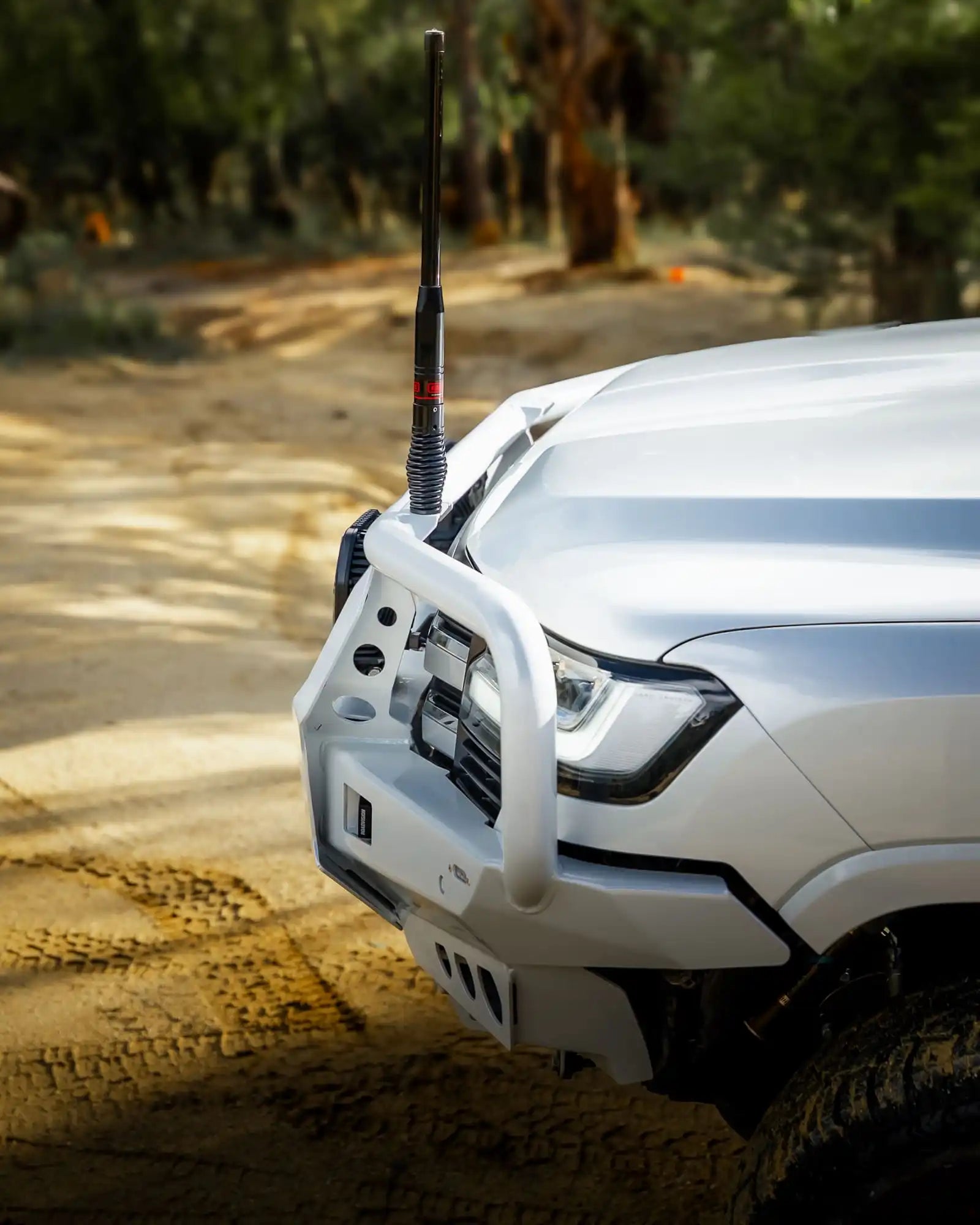 White off-road vehicle with a front bumper and antenna on a dirt road.