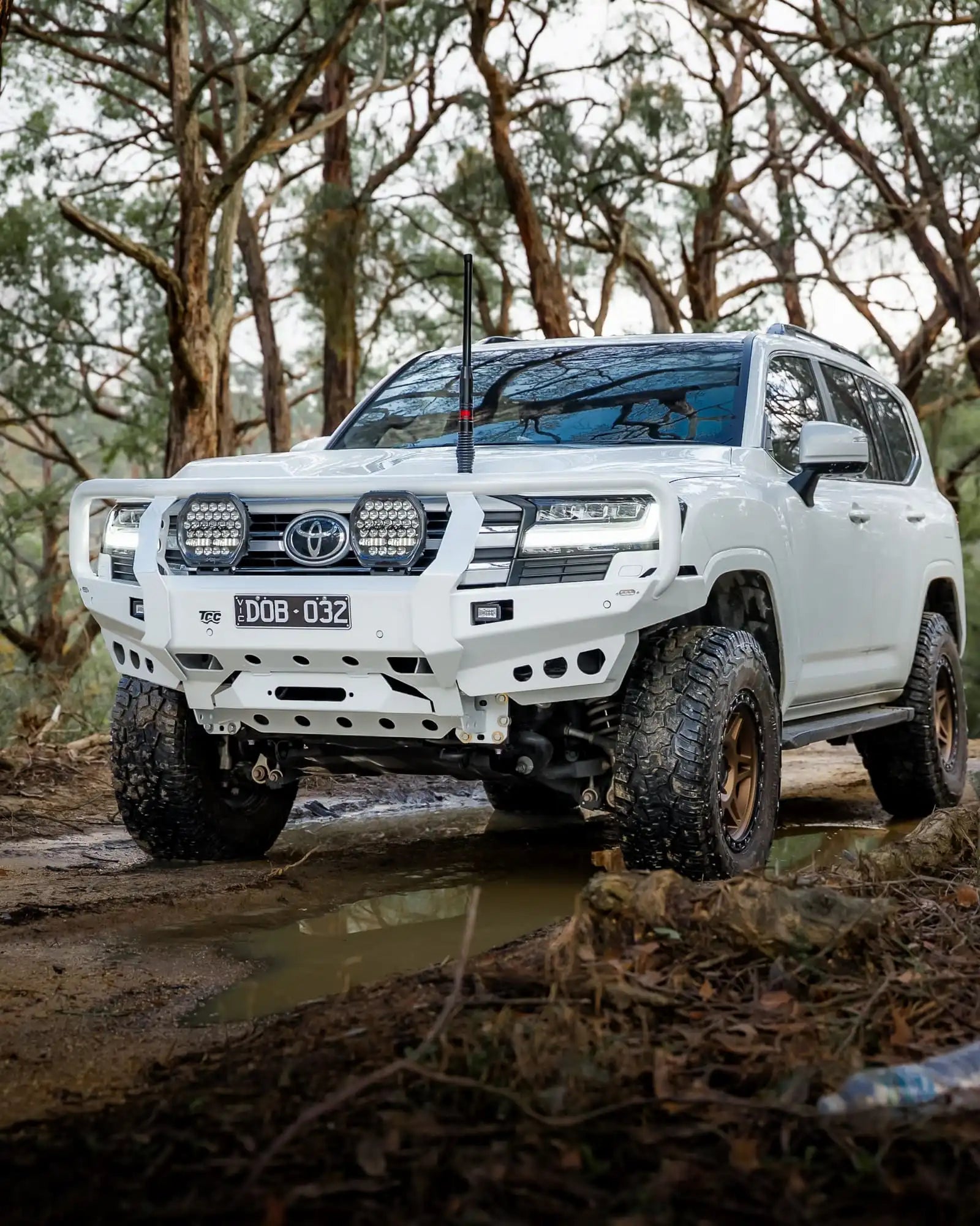 White Toyota SUV driving through a forest on a muddy path