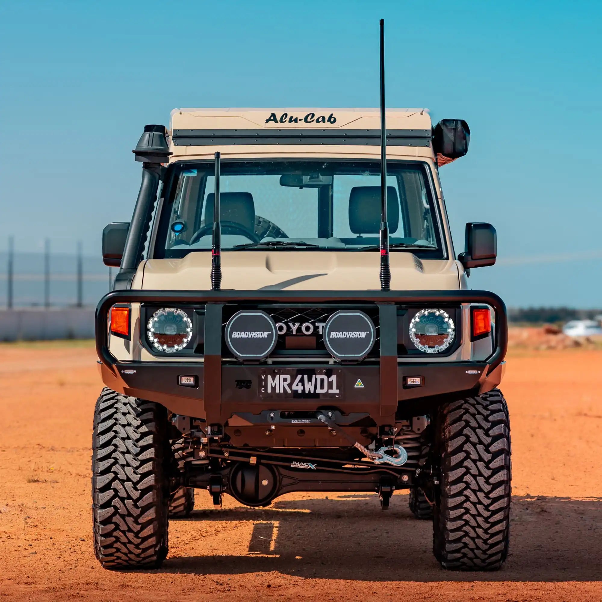 Front view of a rugged off-road vehicle on a dirt road with clear blue sky.
