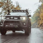 Toyota Hilux driving on a road with trees on both sides with Lazer Lamps Grille Kit for Toyota Hilux (2017-2020)