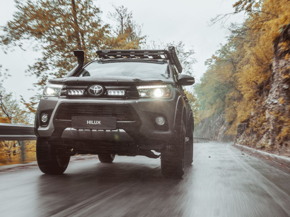 Toyota Hilux driving on a road with trees on both sides with Lazer Lamps Grille Kit for Toyota Hilux (2017-2020)