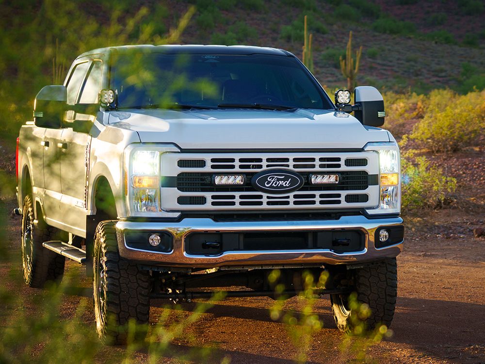 White Ford truck on a dirt road with desert landscape and Lazer Lamps Grille Kit – Ford F-250 & F-350 XL/XLT (2023+)