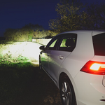 White car parked on a grassy area at night with visible brand logo.