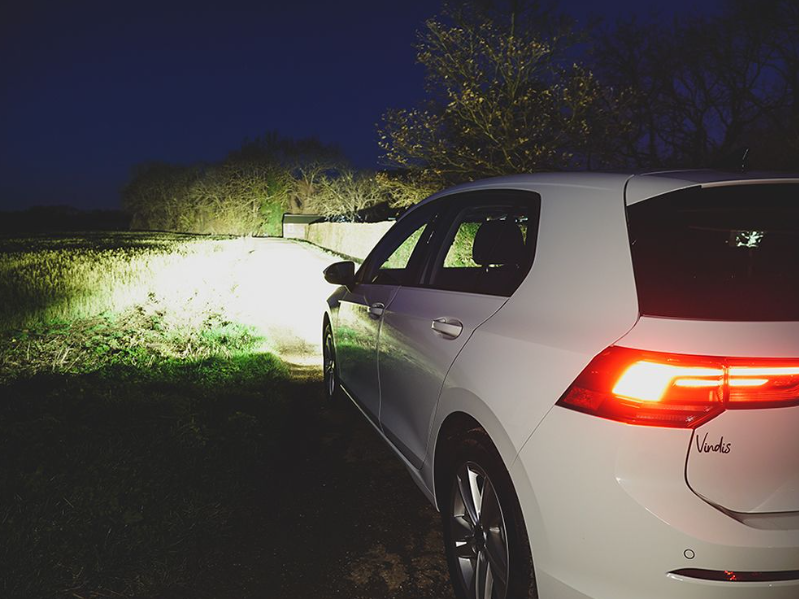 White car parked on a grassy area at night with visible brand logo.