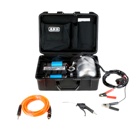 ARB twin piston compressor in its black travel case with the lid open, the twin blue cylinders and polished air tank inside, with the orange hose, blower gun and battery clamp leads laid out in front