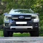 Front view of a Ford vehicle on a road with greenery in the background