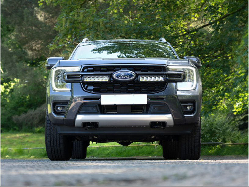 Front view of a Ford vehicle on a road with greenery in the background