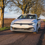 White Volkswagen car on a rural road with trees and fields in the background with Lazer Lamps Grille Kit for VW Golf MK8 (2020–2024)
