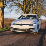 White Volkswagen car on a rural road with trees and fields in the background with Lazer Lamps Grille Kit for VW Golf MK8 (2020–2024)