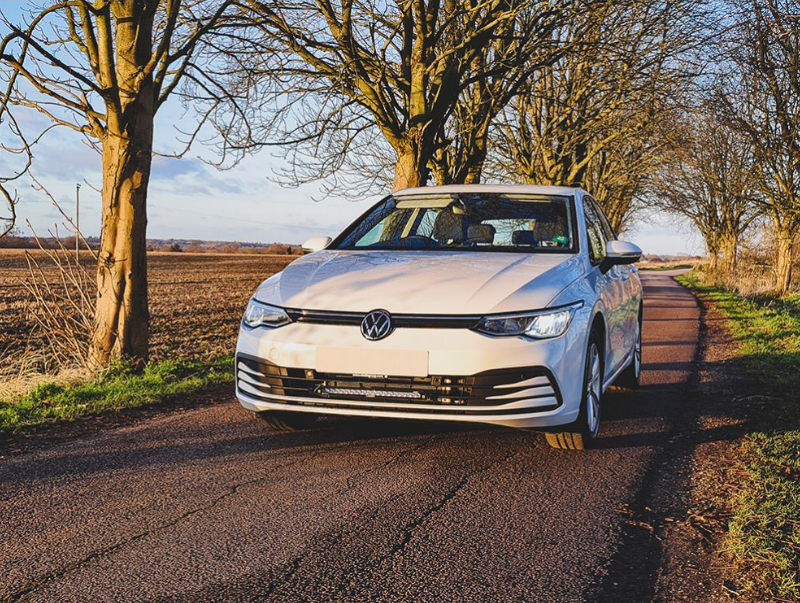 White Volkswagen car on a rural road with trees and fields in the background with Lazer Lamps Grille Kit for VW Golf MK8 (2020–2024)