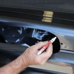 Person using a white marker with red cap on a car door
