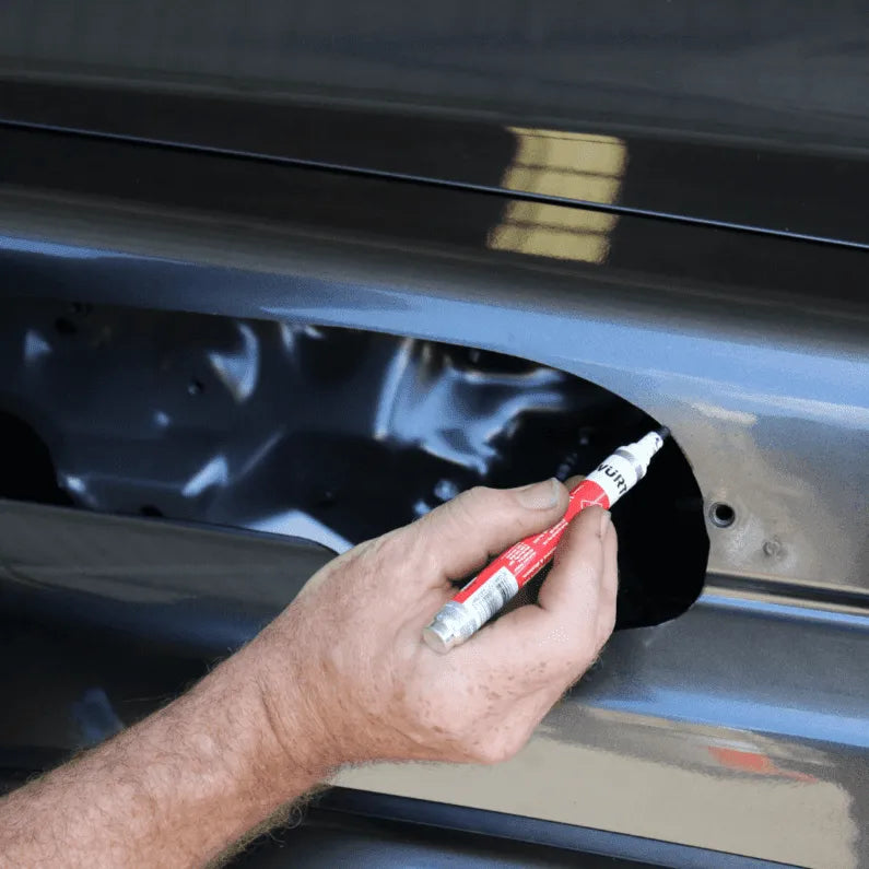 Person using a white marker with red cap on a car door