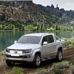Silver Volkswagen Amarok parked on a dirt road with a scenic mountain and lake background