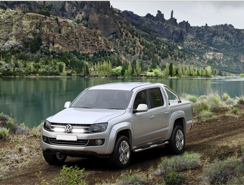Silver Volkswagen Amarok parked on a dirt road with a scenic mountain and lake background