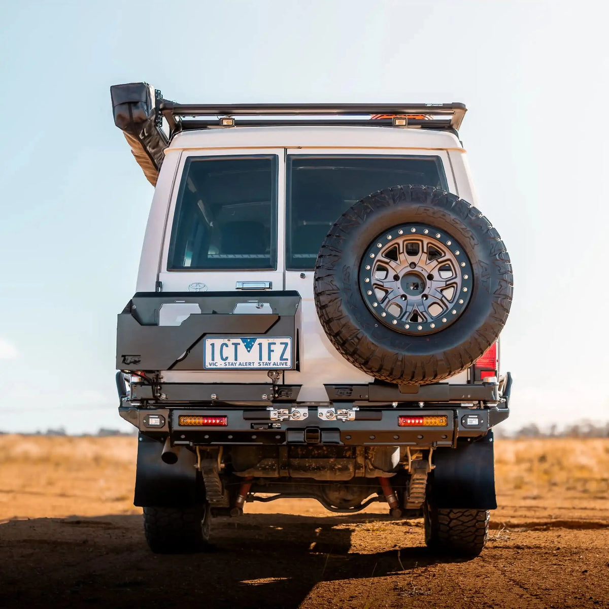 Back view of a rugged vehicle with a spare tire on a dirt road – TCC 78 Series Troop carrier Rear Bar Tow Bar