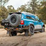 Blue SUV with spare tire on a dirt road surrounded by trees