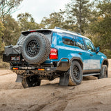 Blue SUV with spare tire on a dirt road surrounded by trees