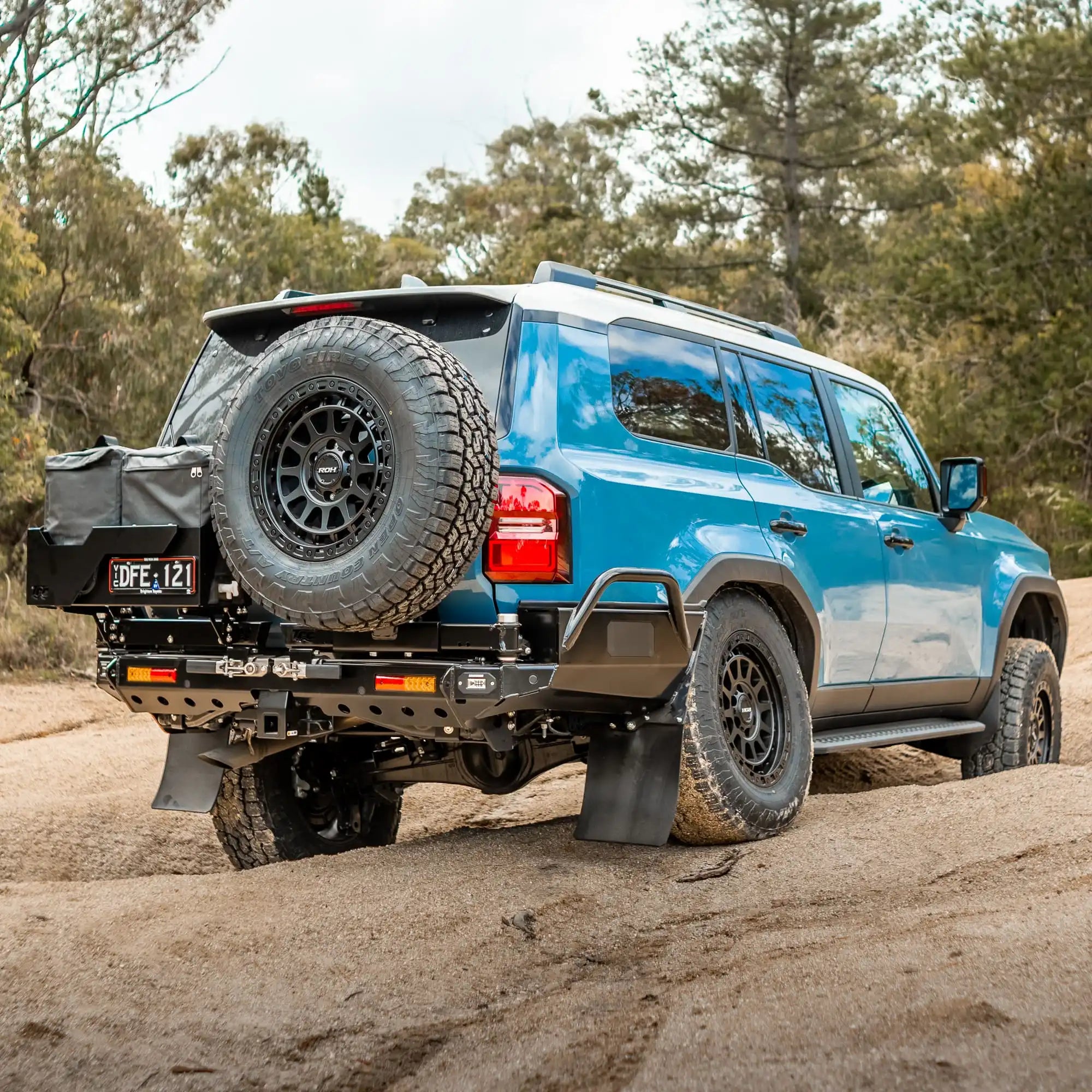 Blue SUV with spare tire on a dirt road surrounded by trees