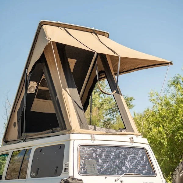 White SUV with a beige rooftop tent set against a clear blue sky.