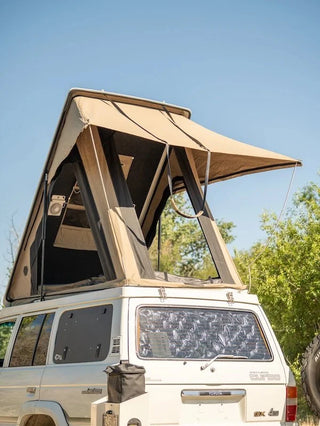White SUV with a beige rooftop tent set against a clear blue sky.