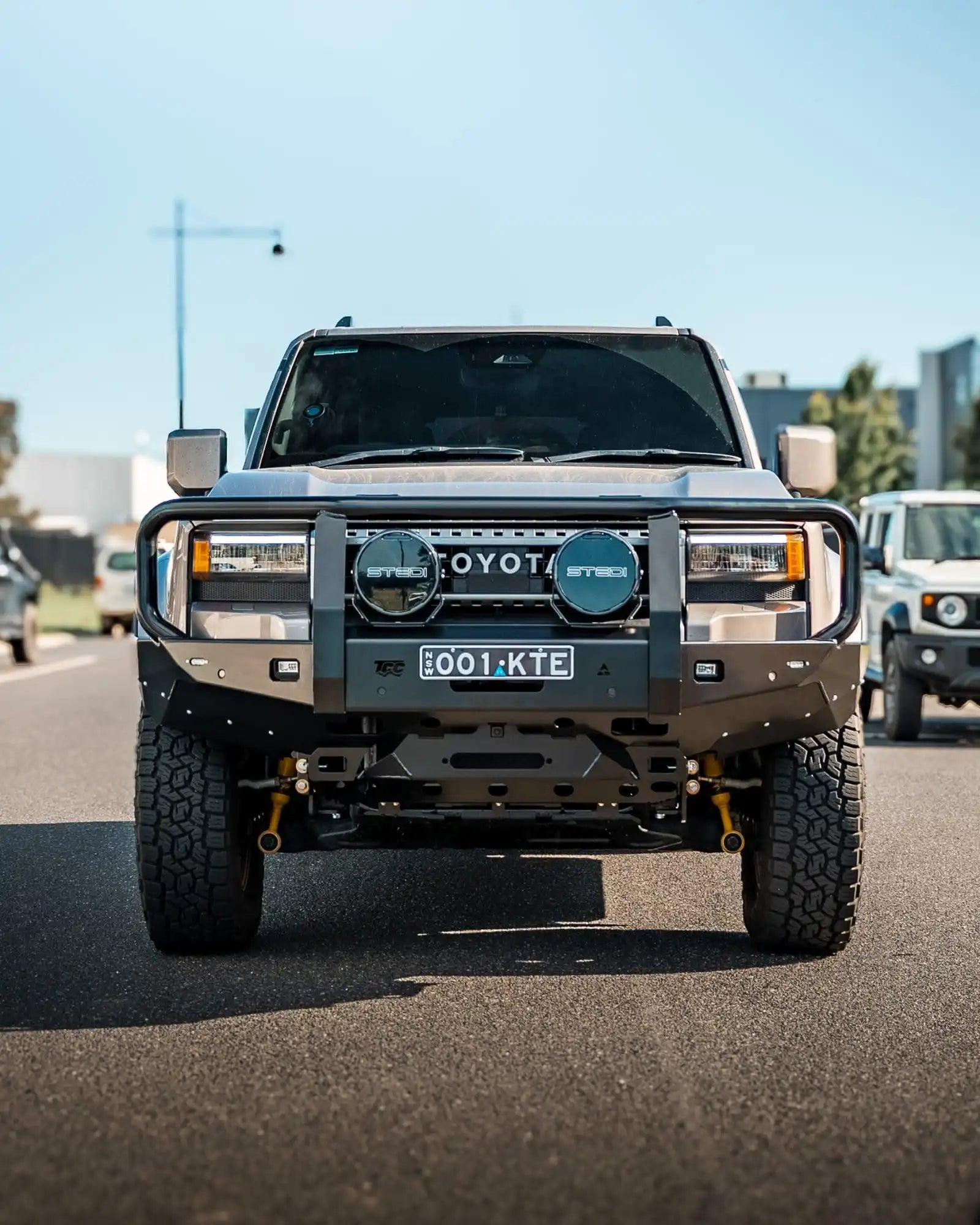 Toyota prado 250 with large front grille and off-road tires on a road.
