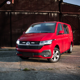 Red Volkswagen van parked in front of a rustic metal building.