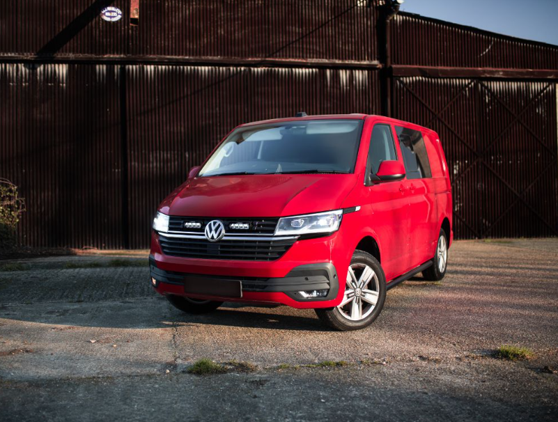 Red Volkswagen van parked in front of a rustic metal building.