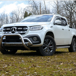 White Mercedes-Benz truck on a grassy field with trees in the background