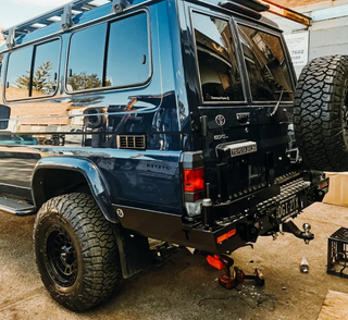 Blue off-road vehicle with large tires and Thorburns LC75/78 Rear Bar on a concrete surface.