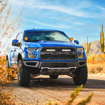 Blue F150 raptor truck on a desert road with cacti and mountains in the background with Lazer Lamps Grille Kit – Ford F-150 Raptor (2017–2020)
