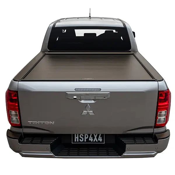 Back view of a silver Mitsubishi Triton pickup truck with a tonneau cover on a white background