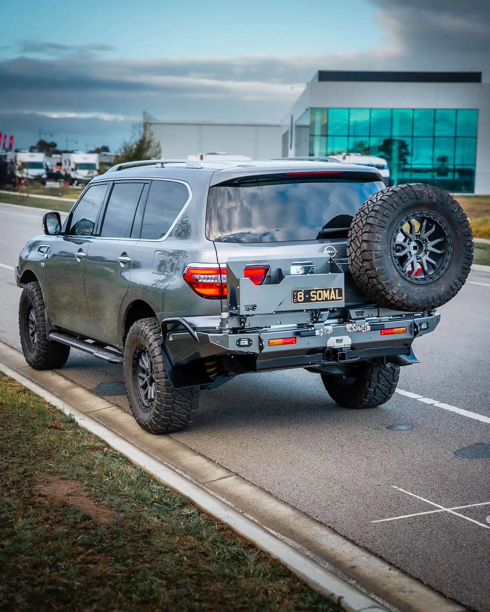Silver SUV with off-road tires on a road near a building