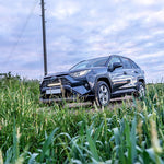 SUV driving through a grassy field with a cloudy sky with Lazer Lamps Grille Kit for Toyota RAV4 Hybrid (2019+)