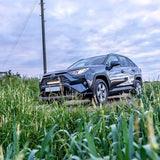 SUV driving through a grassy field with a cloudy sky with Lazer Lamps Grille Kit for Toyota RAV4 Hybrid (2019+)