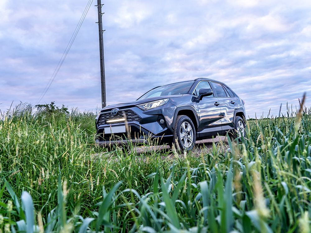 SUV driving through a grassy field with a cloudy sky with Lazer Lamps Grille Kit for Toyota RAV4 Hybrid (2019+)