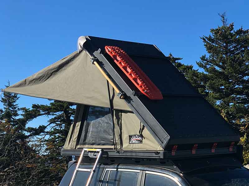 Bush Company AX27 Clamshell Rooftop Tent attached to a vehicle with trees in the background