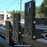 Adjustable awning brackets on a vehicle roof with a blurred background of trees and buildings.
