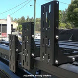 Adjustable awning brackets on a vehicle roof with a blurred background of trees and buildings.