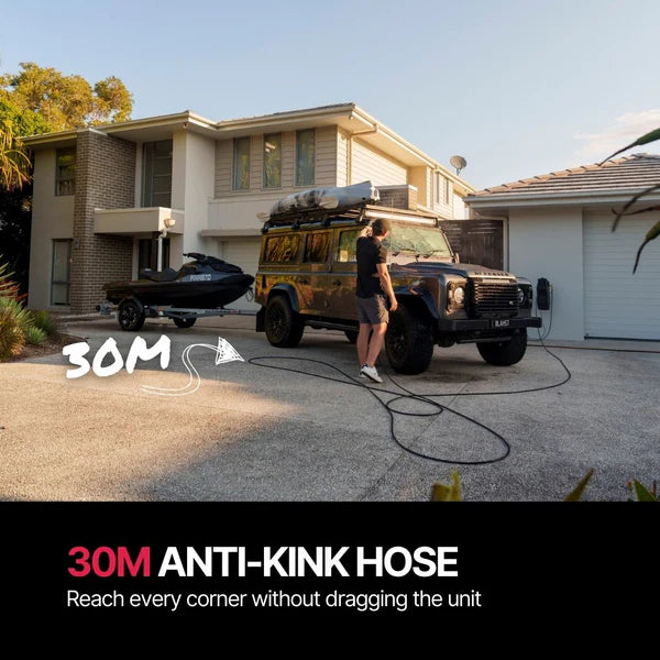 Person using a long hose to clean a vehicle in front of a house