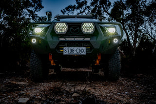 Front view of a green Mazda BT-50 at dusk with a pair of Lightforce BEAST driving lights illuminated on the bullbar