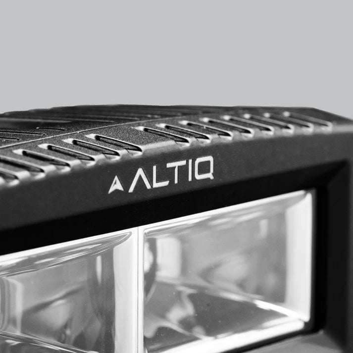 Close-up of the top edge of an ALTIQ CX4 light, the ALTIQ name and arrow set into the ribbed cooling fins above the clear lens and its reflector segments