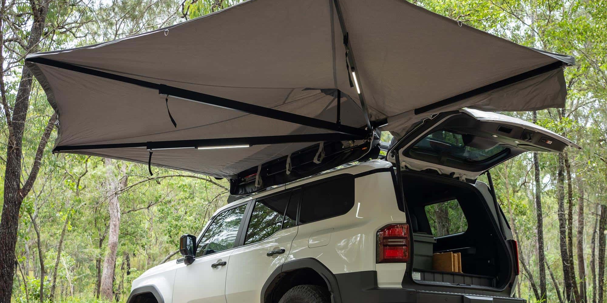 Car with an extended roof tent in a forest setting with Destination 4WD 180 Degree Freestanding Awning Swing to the rear