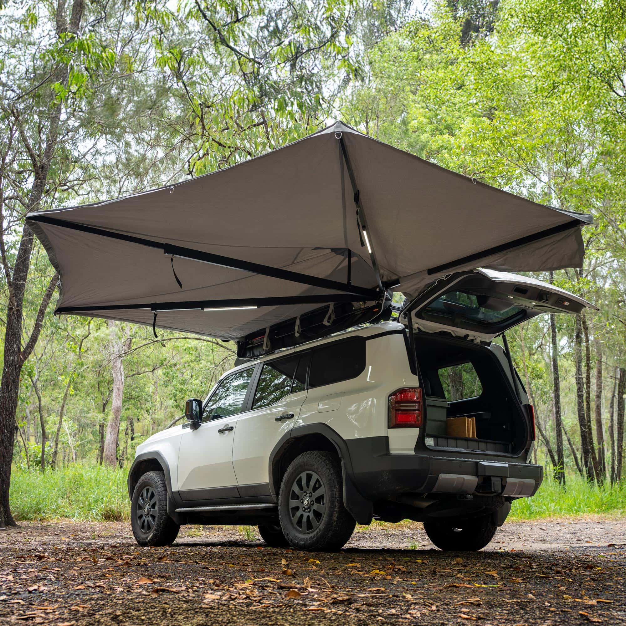 Car with an extended roof tent in a forest setting with Destination 4WD 180 Degree Freestanding Awning Swing to the rear