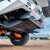 Close-up of a vehicle's undercarriage with visible suspension and tires on a dirt surface.
