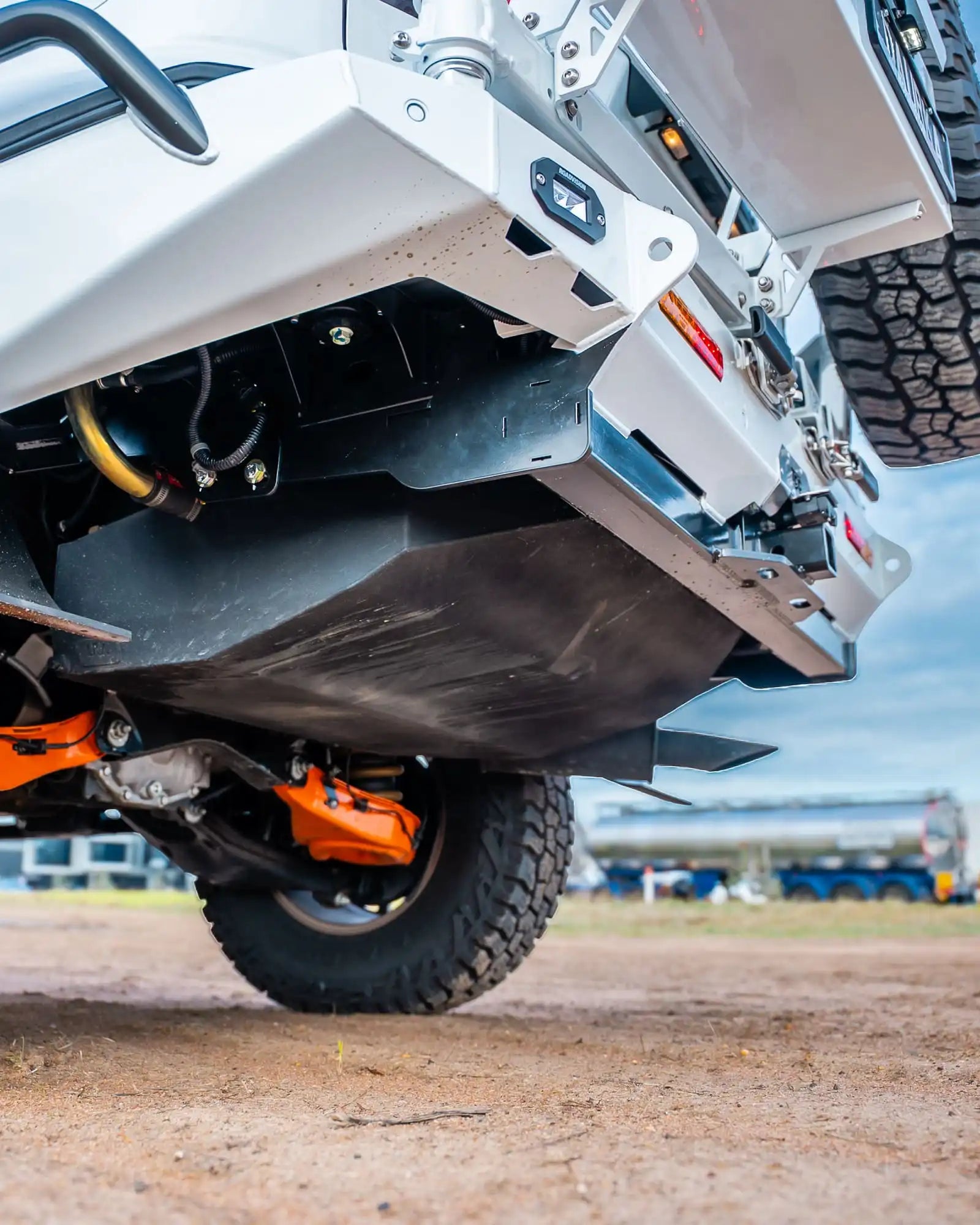 Close-up of a vehicle's undercarriage with visible suspension and tires on a dirt surface.