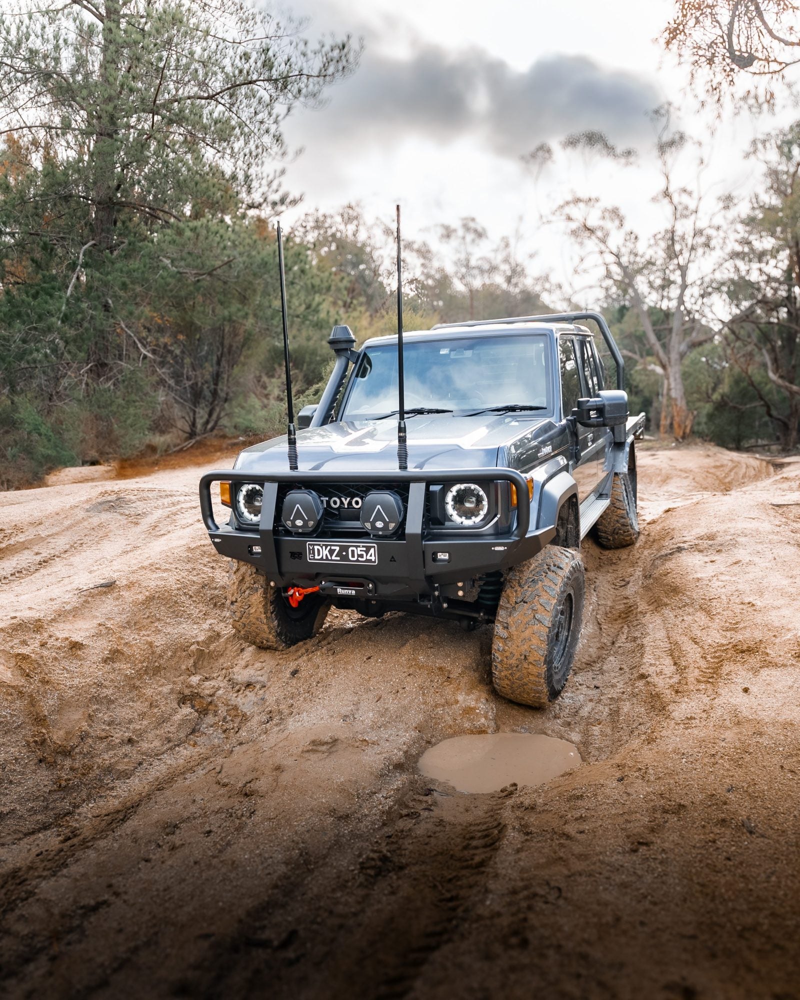 Off-road vehicle driving on a muddy path with trees in the background