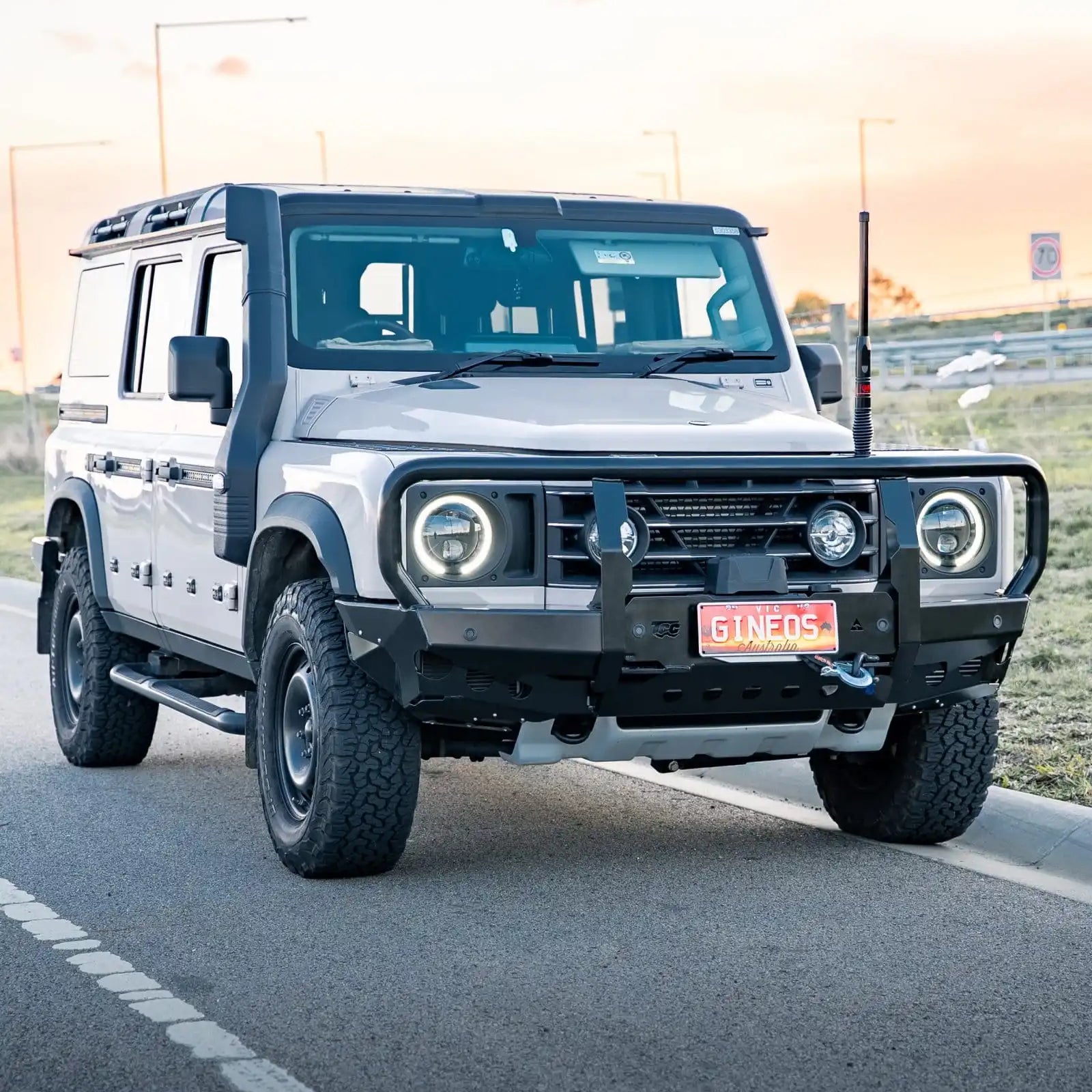 White off-road vehicle on a road with a sunset in the background