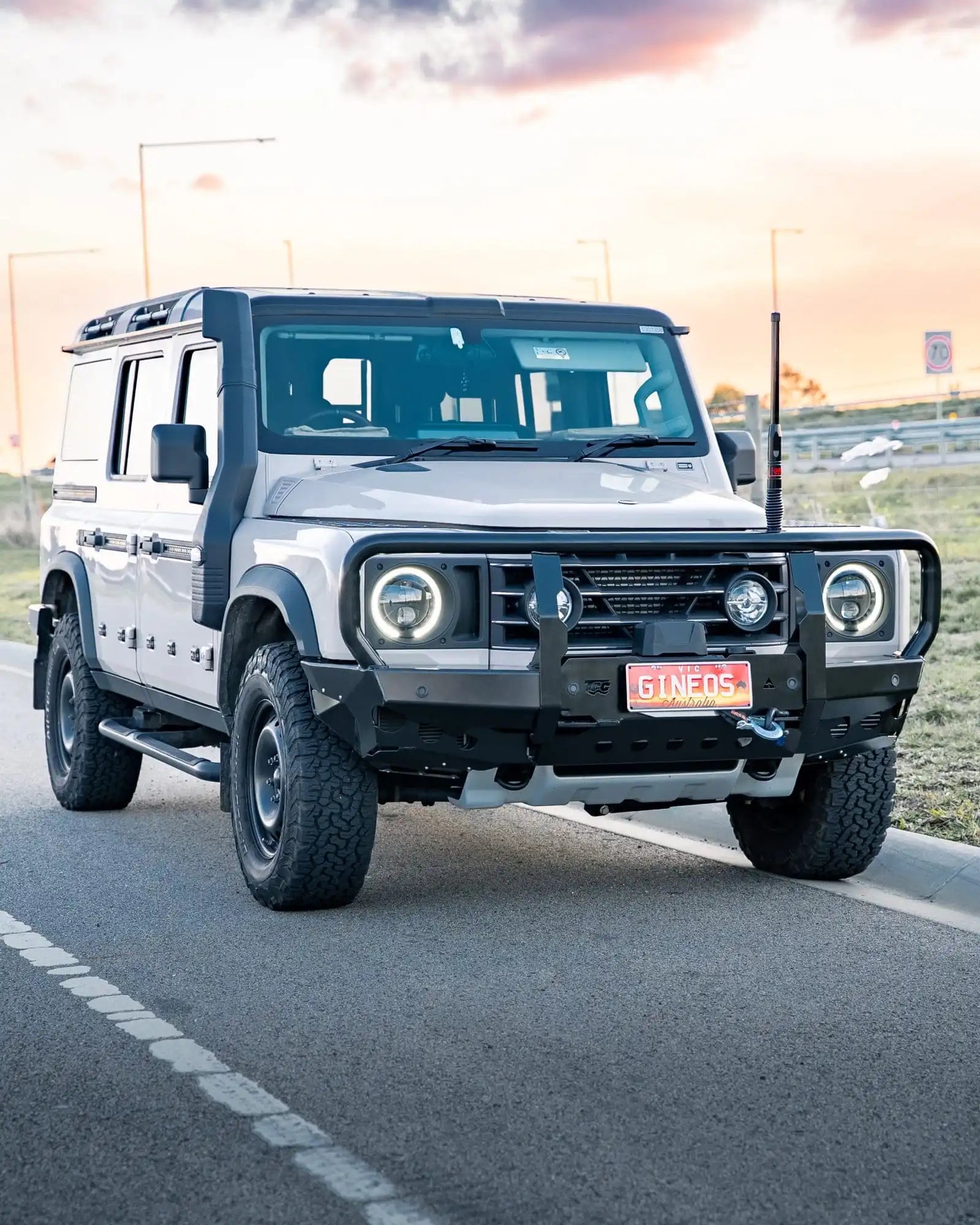 White off-road vehicle on a road with a sunset in the background